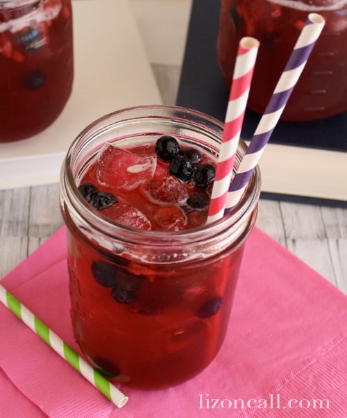 a glass of fresh fruit punch garnished with fresh berries and striped paper straws